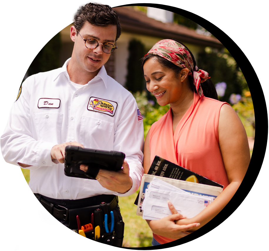 Electrician in uniform showing a customer a tablet, smiling, and standing in front of a home.